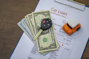 Car keys, cash and a toy car on top of a car loan application.
