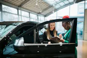 A woman signs paperwork next to her new car.